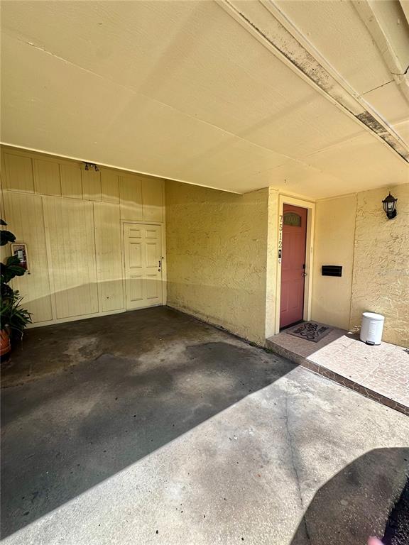 A covered concrete carport leads to a red front door with a small welcome mat — 7512 BOLANOS COURT UNIT 7512, TAMPA, FL