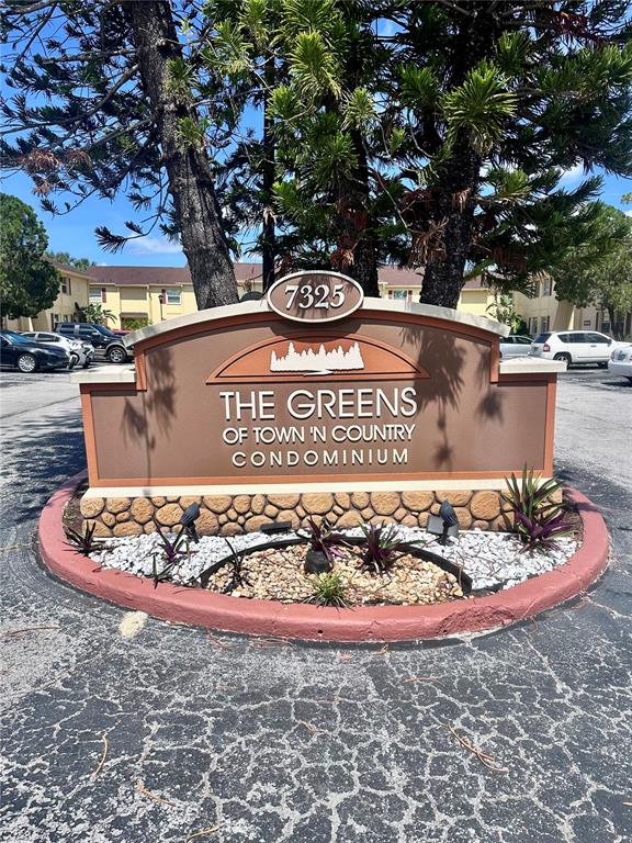 A brown monument sign for The Greens of Town 'N Country Condominium stands outdoors — 7512 BOLANOS COURT UNIT 7512, TAMPA, FL