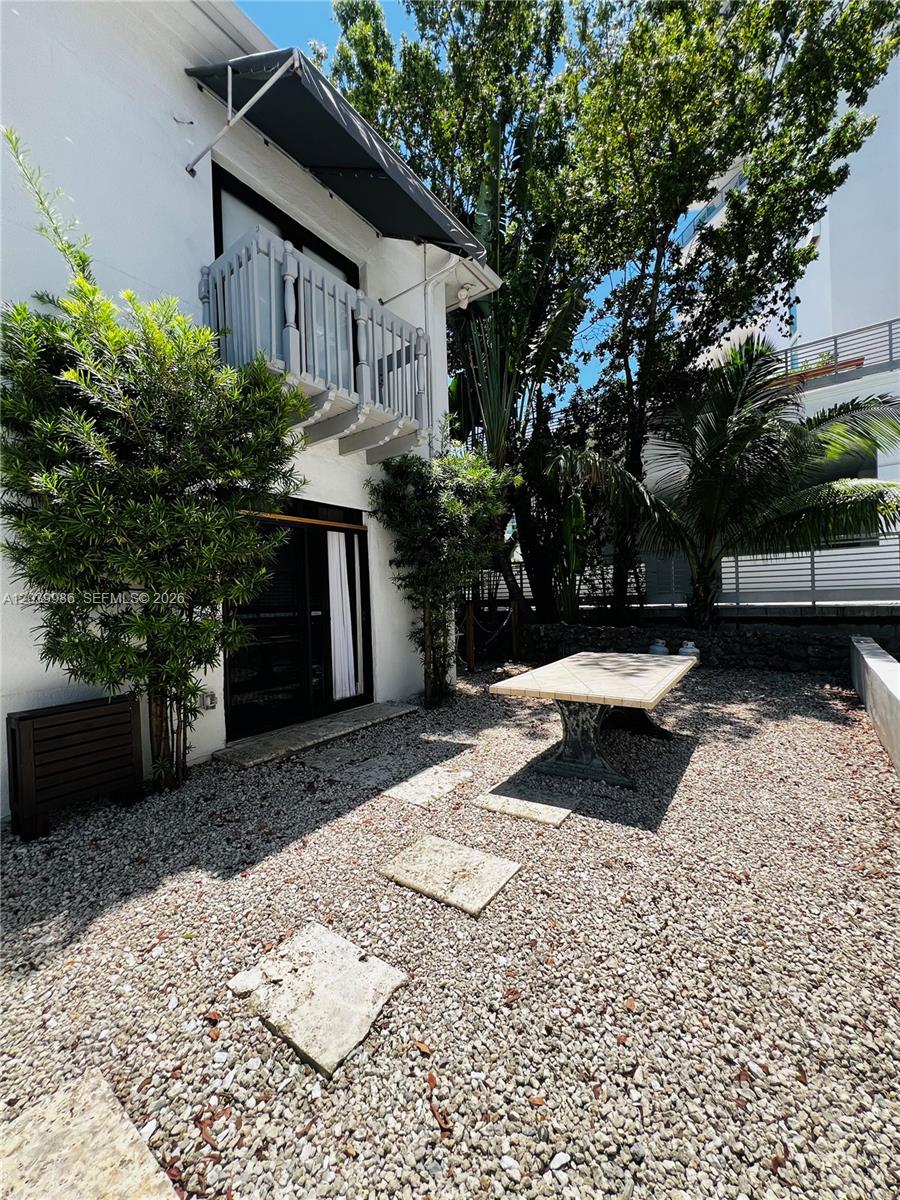 A gravel patio features a stone table, a small tree, and a balcony above — 1470 Lincoln Ter # 2, Miami Beach FL 33139, MIAMI BEACH, FL