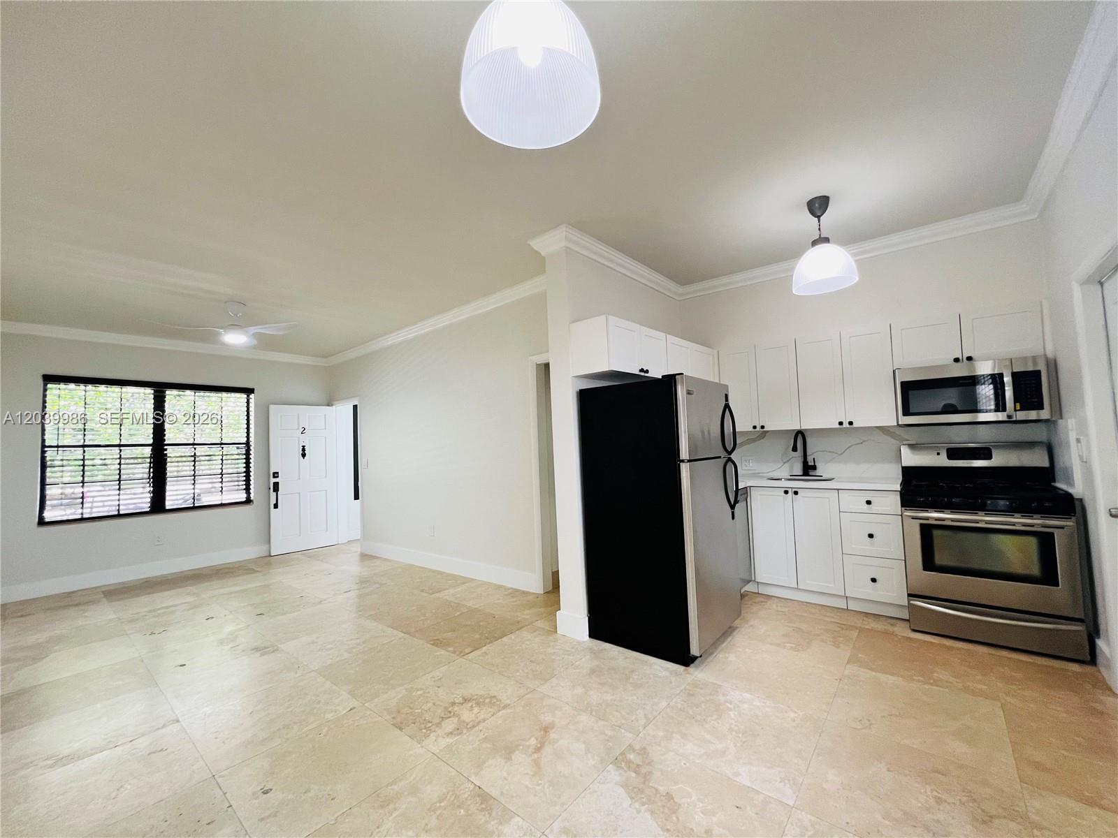 An open-concept kitchen and living area features white cabinets, stainless steel appliances, and tile flooring — 1470 Lincoln Ter # 2, Miami Beach FL 33139, MIAMI BEACH, FL
