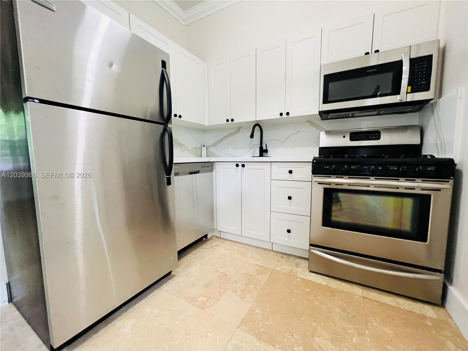 A kitchen features white cabinets, stainless steel appliances, a marble-style backsplash, and light-colored tile flooring — 1470 Lincoln Ter # 2, Miami Beach FL 33139, MIAMI BEACH, FL