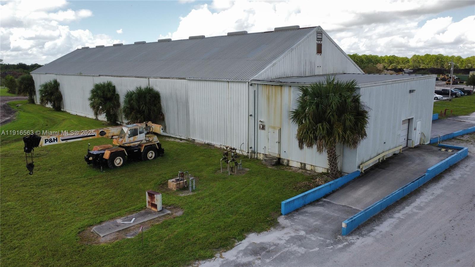 An aerial view of a large metal warehouse with a crane parked on the lawn — 925 SW 74th Ave SW, FL 32968, FL