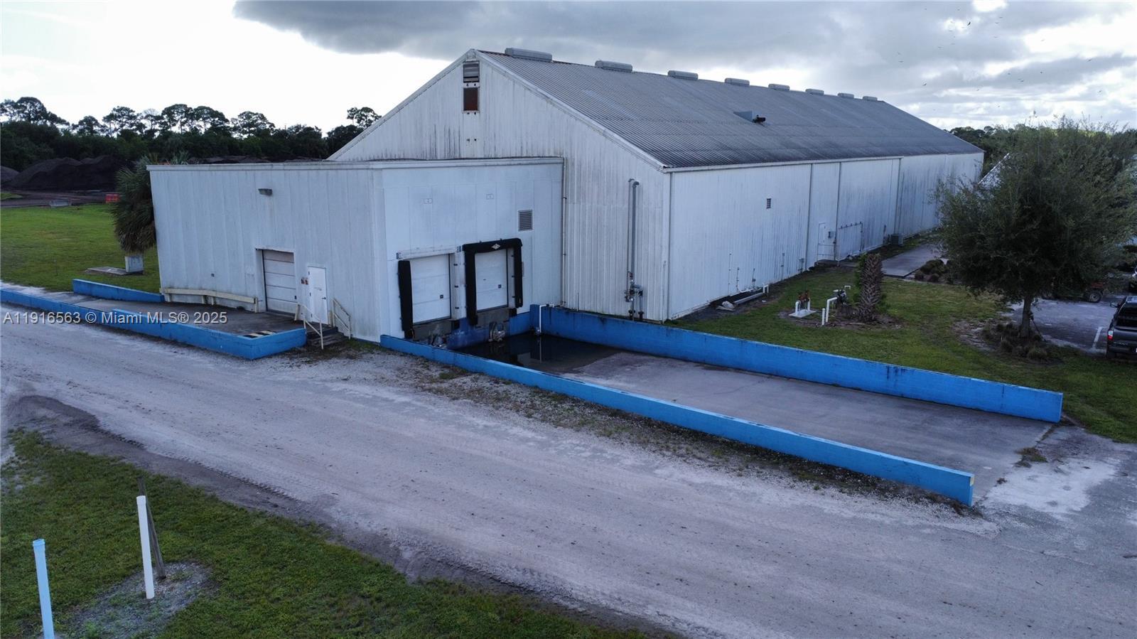 An aerial view shows a white metal warehouse with a recessed loading dock area — 925 SW 74th Ave SW, FL 32968, FL