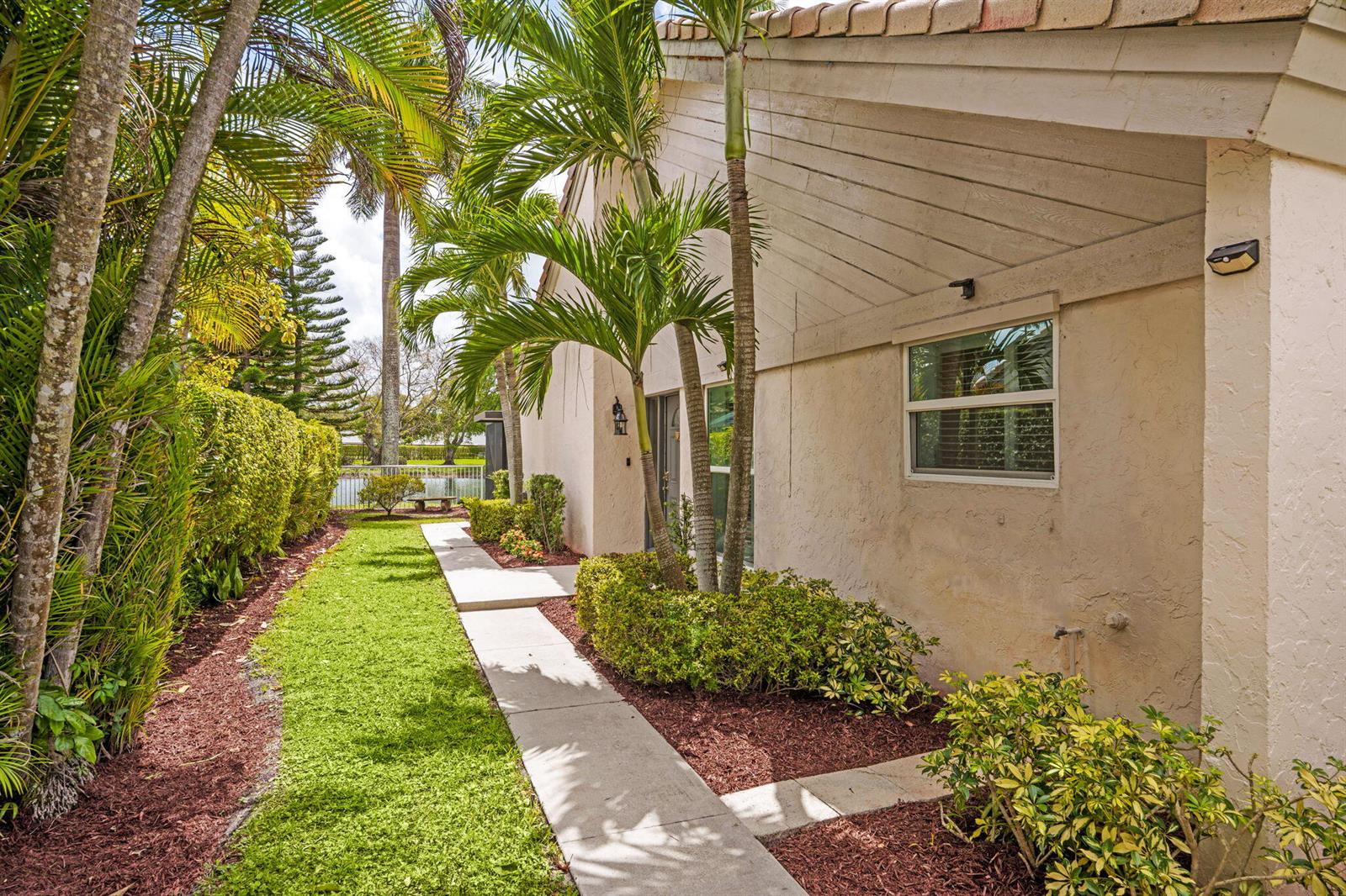 A concrete walkway leads along the side of a beige house with palm trees — 9722 Erica Court, Boca Raton FL 33496, BOCA RATON, FL