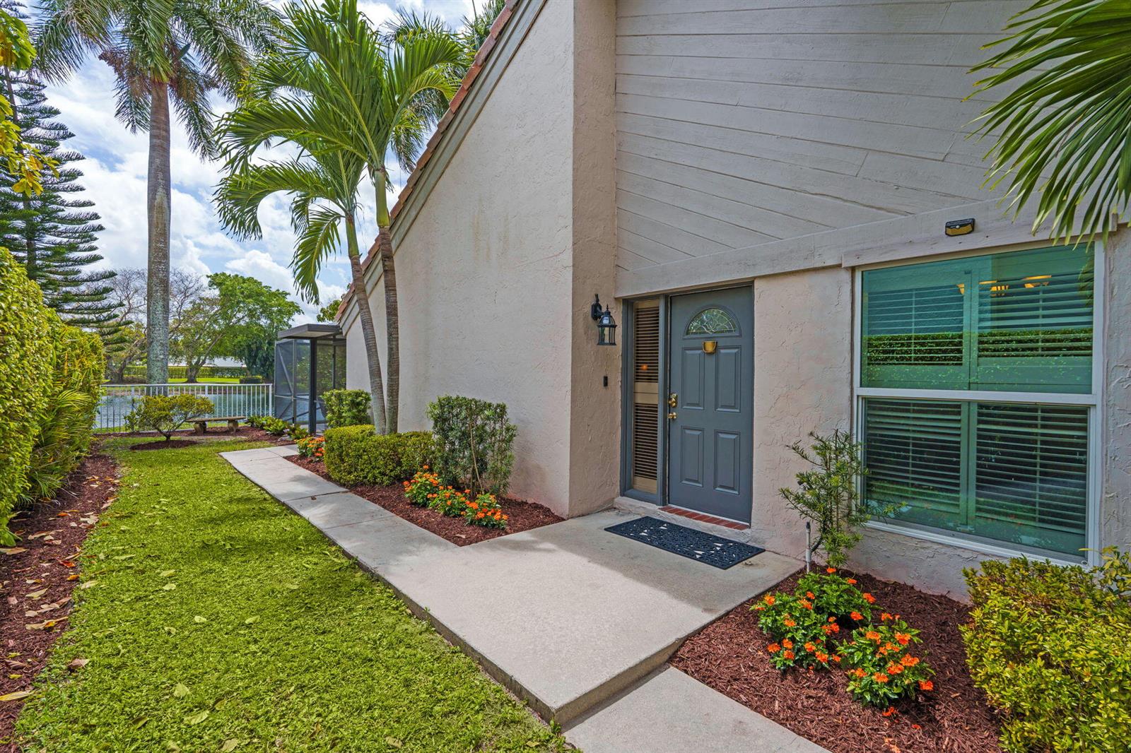 A concrete walkway leads to the front entrance of a house with a gray door — 9722 Erica Court, Boca Raton FL 33496, BOCA RATON, FL