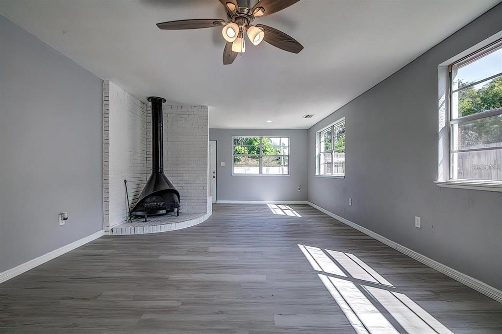 A living room with gray walls, wood-look flooring, a ceiling fan, and a corner fireplace — 2107 MONTICELLO AVENUE, LAKELAND, FL