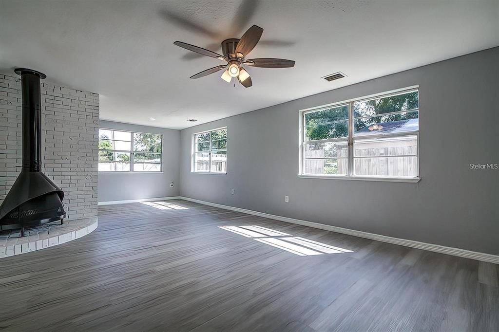 A living room features gray walls, wood-look flooring, a ceiling fan, and a brick fireplace — 2107 MONTICELLO AVENUE, LAKELAND, FL