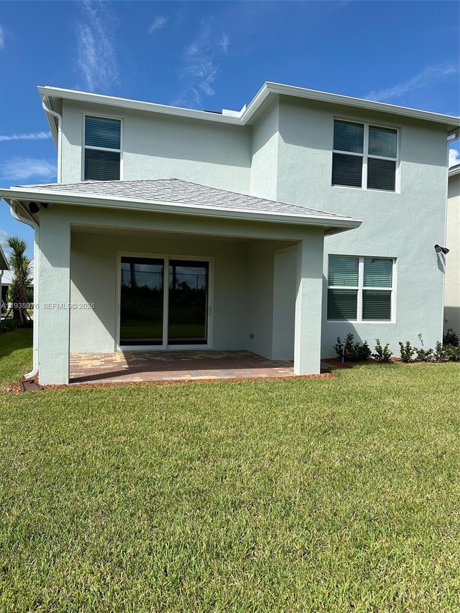The rear exterior of a two-story house features a covered patio and a grassy yard — PORT ST. LUCIE, FL
