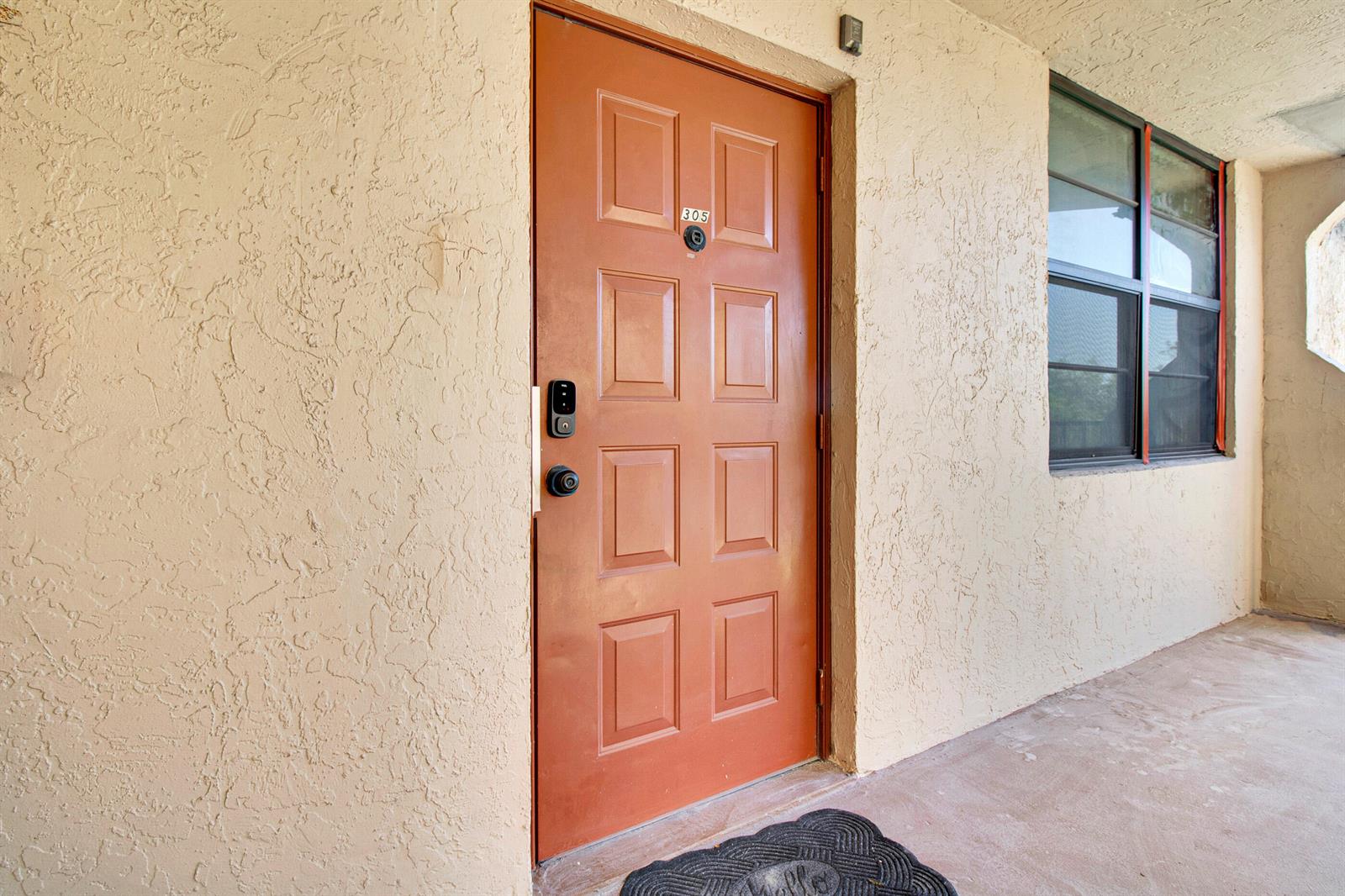 A brown front door with a digital lock and peephole sits on a textured exterior wall — 3450 Blue Lake Drive # 305, Pompano Beach FL 33064, POMPANO BEACH, FL