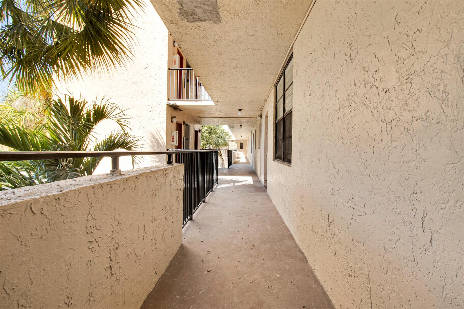 An outdoor apartment complex walkway with a concrete floor, stucco walls, and metal railings — 3450 Blue Lake Drive # 305, Pompano Beach FL 33064, POMPANO BEACH, FL