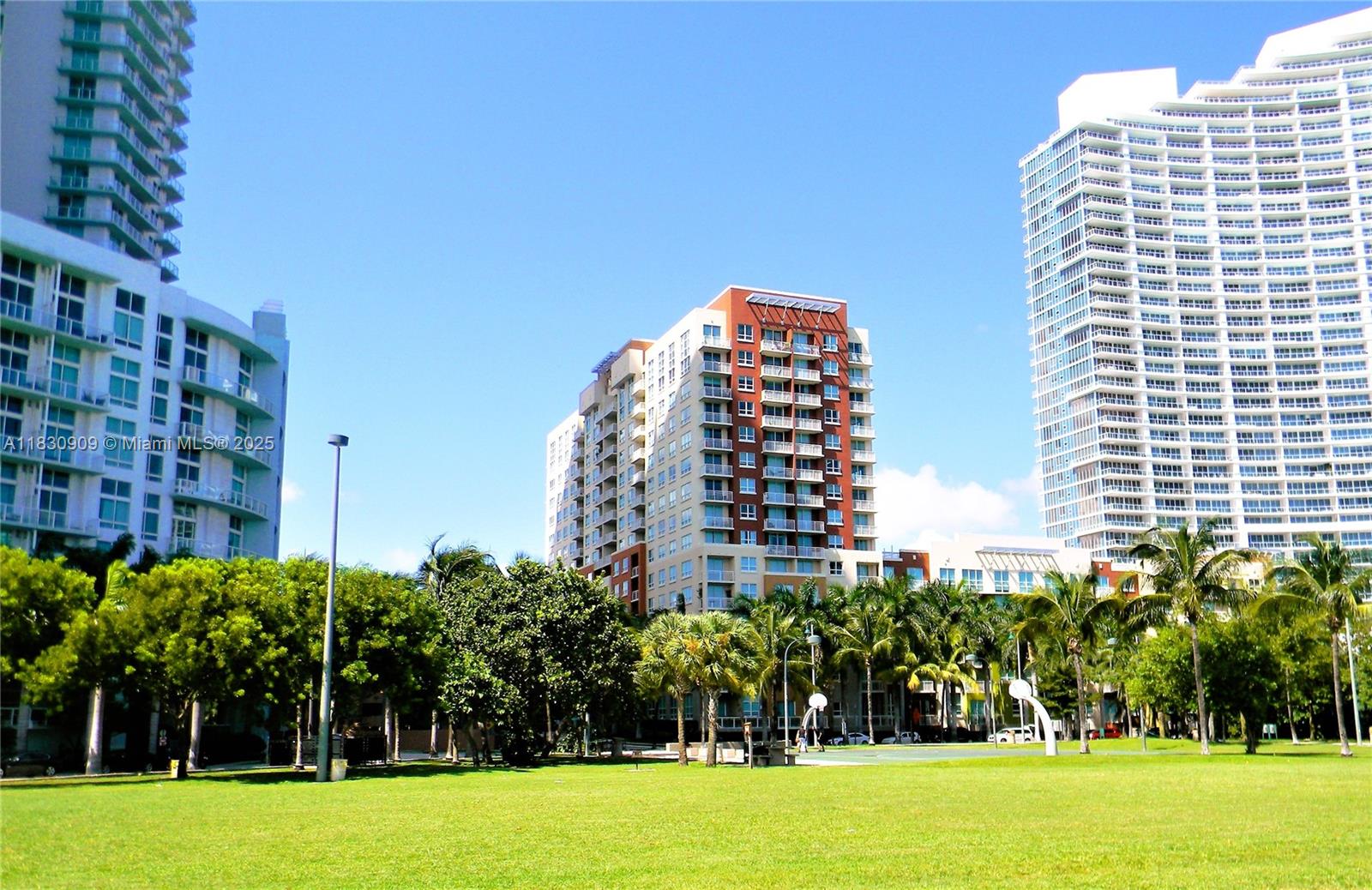 A grassy park sits in front of three tall apartment buildings under a clear sky — 2000 N Bayshore Dr # 509, Miami FL 33137, MIAMI, FL
