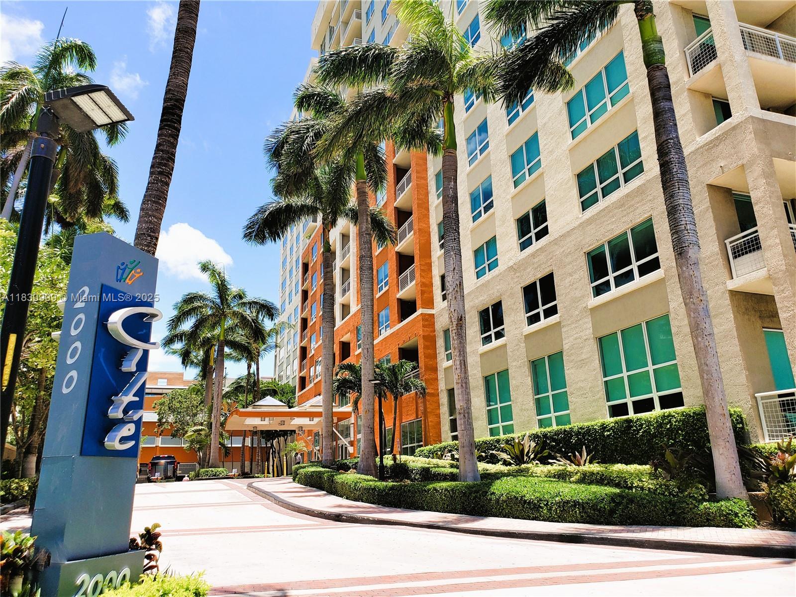 A tall blue sign stands in front of a multi-story apartment building with palm trees — 2000 N Bayshore Dr # 509, Miami FL 33137, MIAMI, FL