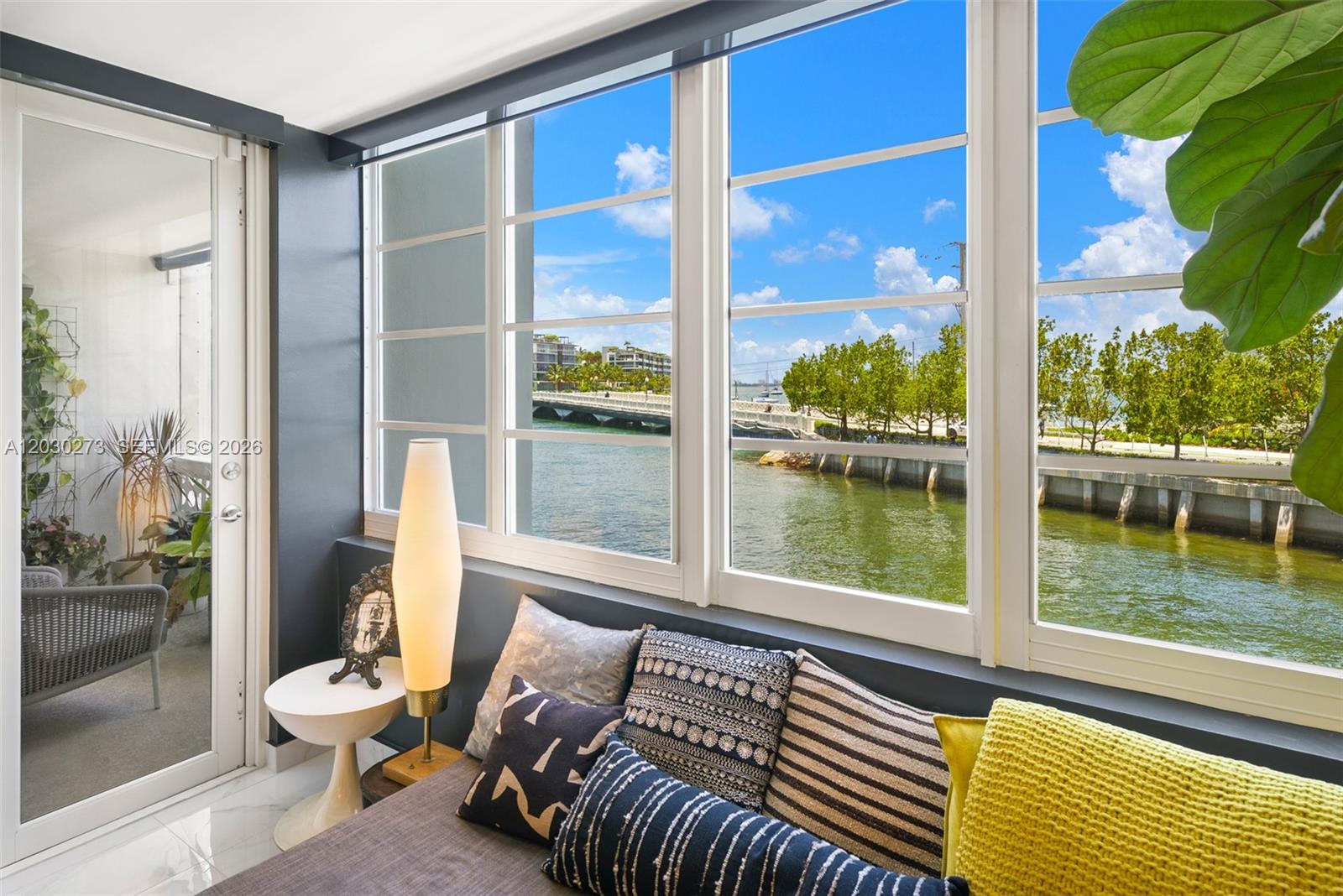 A sunroom features a gray sofa, a floor lamp, and large windows overlooking a bridge — 1670 Lincoln Ct # 2B, Miami Beach FL 33139, MIAMI BEACH, FL