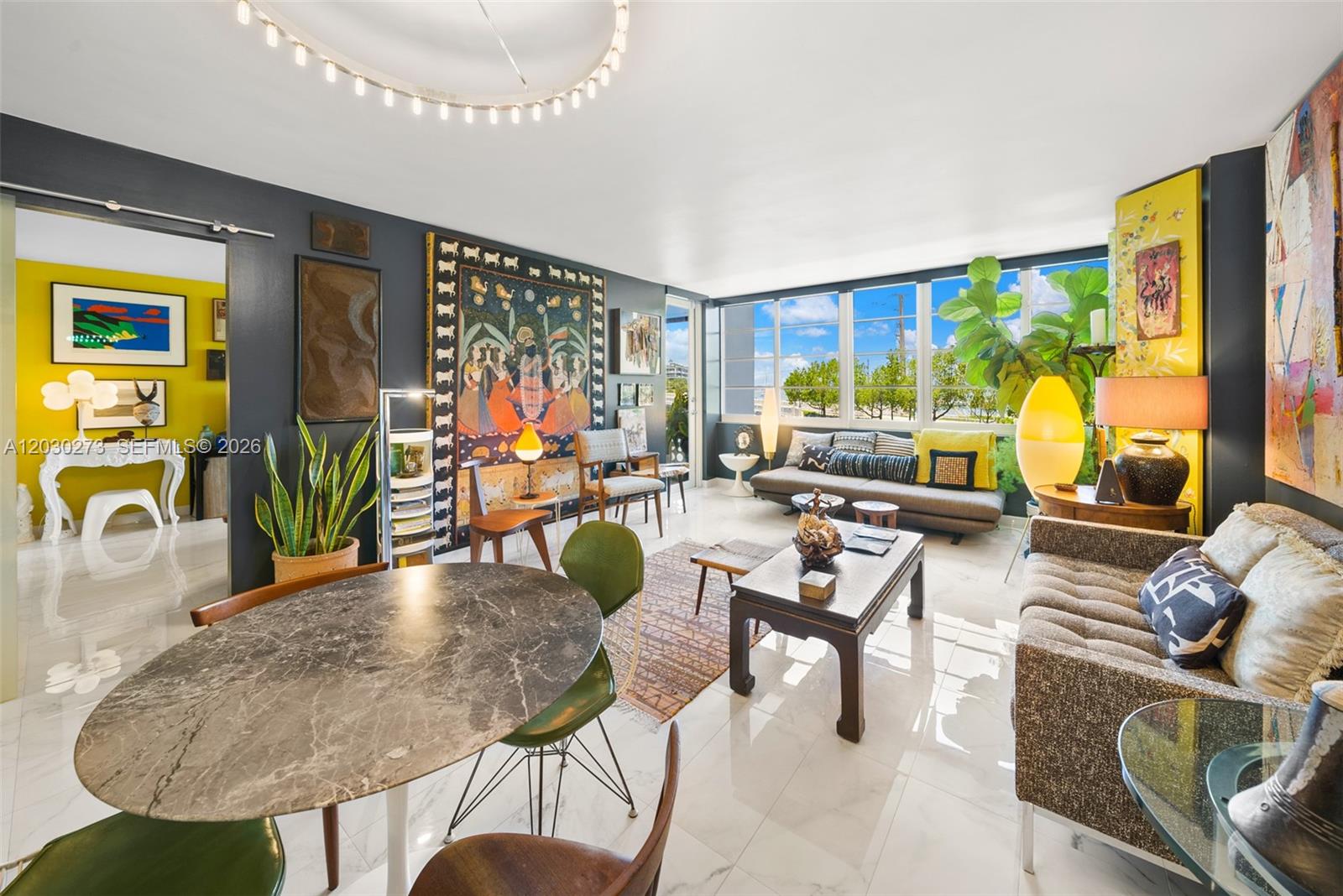 A living and dining area features dark walls, marble floors, eclectic art, and large windows — 1670 Lincoln Ct # 2B, Miami Beach FL 33139, MIAMI BEACH, FL