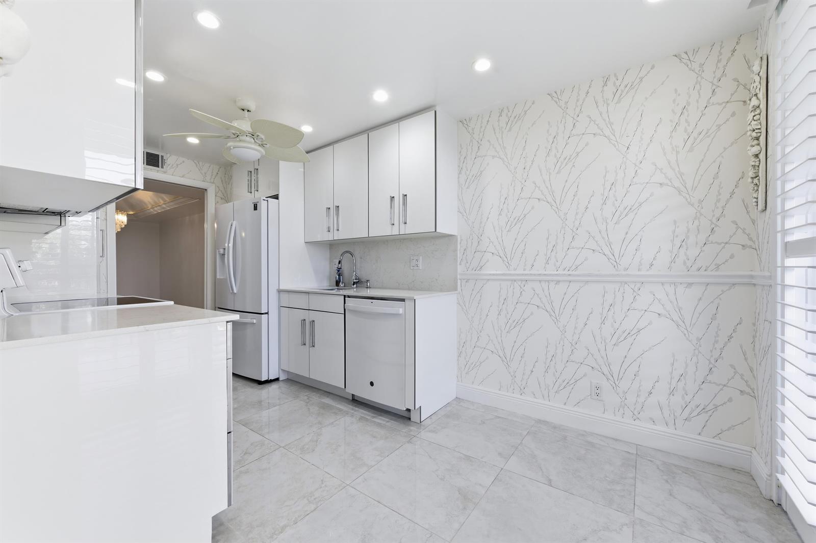 A white kitchen features modern cabinetry, stainless steel appliances, and patterned wallpaper above a chair rail — 2778 S Ocean Boulevard # 206s, Palm Beach FL 33480, PALM BEACH, FL