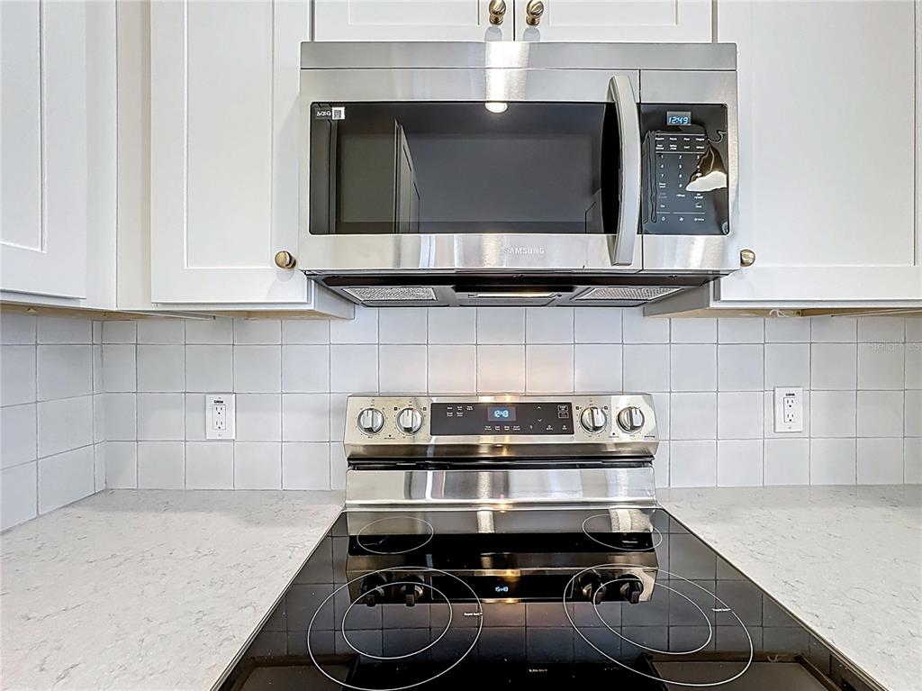 A stainless steel microwave and electric range are installed between white cabinets and tiled backsplash — 1018 DOWD AVENUE, ORLANDO, FL