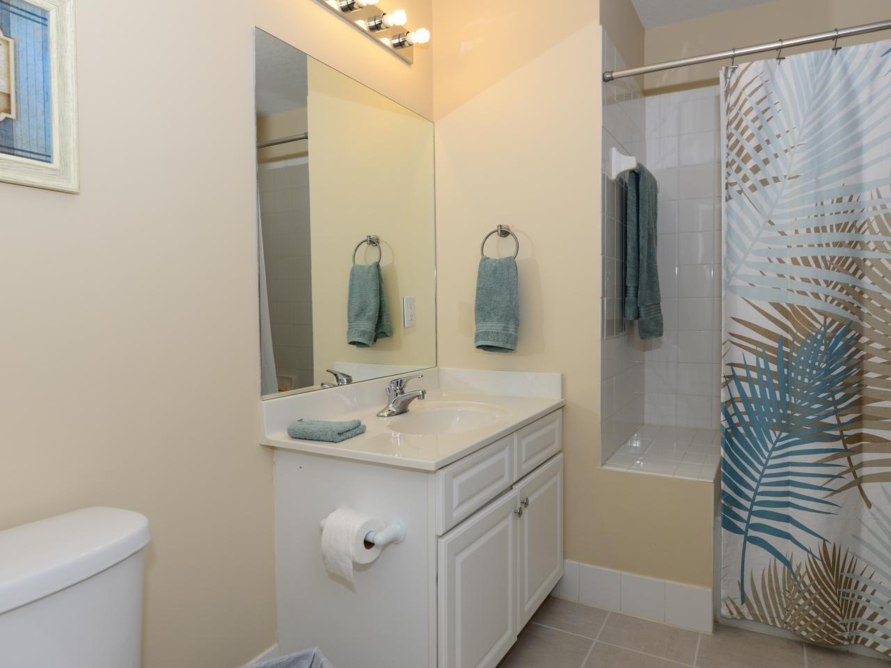 A bathroom features a white vanity, a large mirror, and a shower with a palm-patterned curtain — 1200 Town Center Drive # 216, Jupiter FL 33458, JUPITER, FL