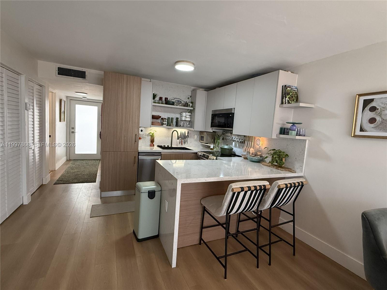 A modern kitchen features light wood cabinetry, white countertops, a breakfast bar, and striped stools — 1666 West Ave # 305, Miami Beach FL 33139, MIAMI BEACH, FL