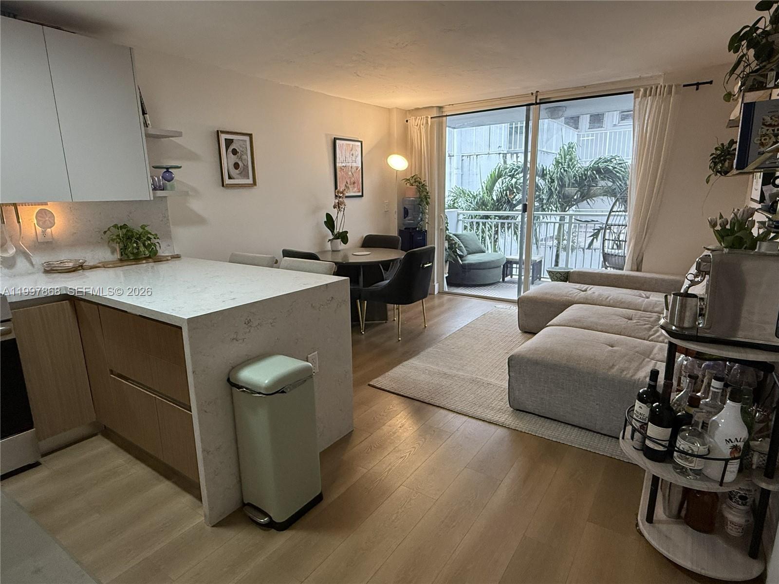 An open-concept living and dining area features a kitchen island, light wood floors, and balcony — 1666 West Ave # 305, Miami Beach FL 33139, MIAMI BEACH, FL