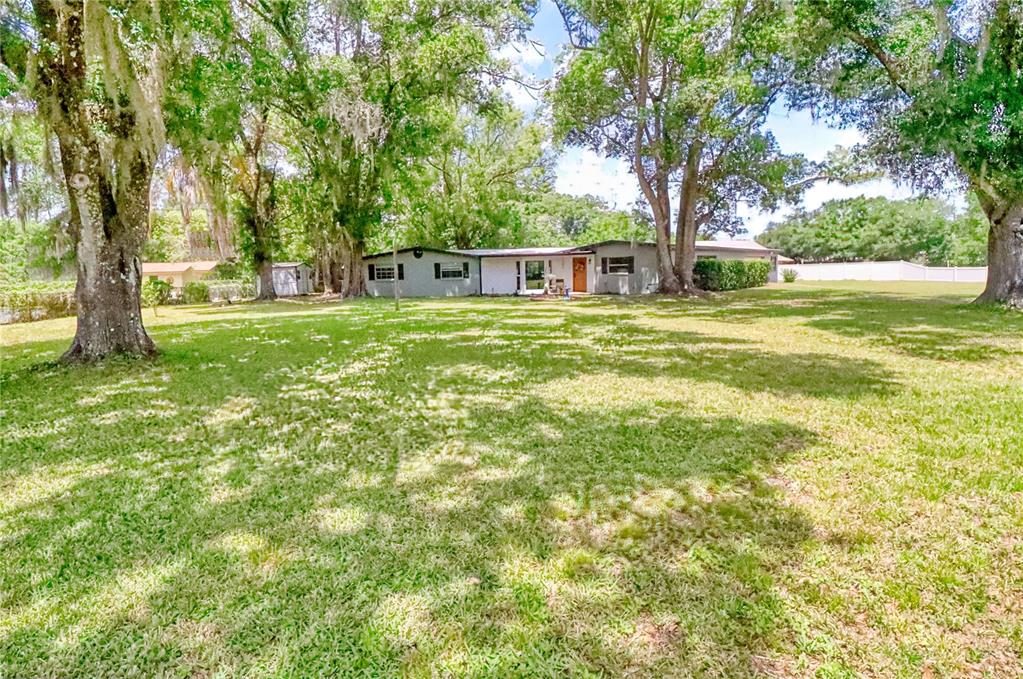 A single-story house with a gray exterior sits on a large, tree-shaded grassy lot — 5205 FIVE ACRE ROAD, PLANT CITY, FL