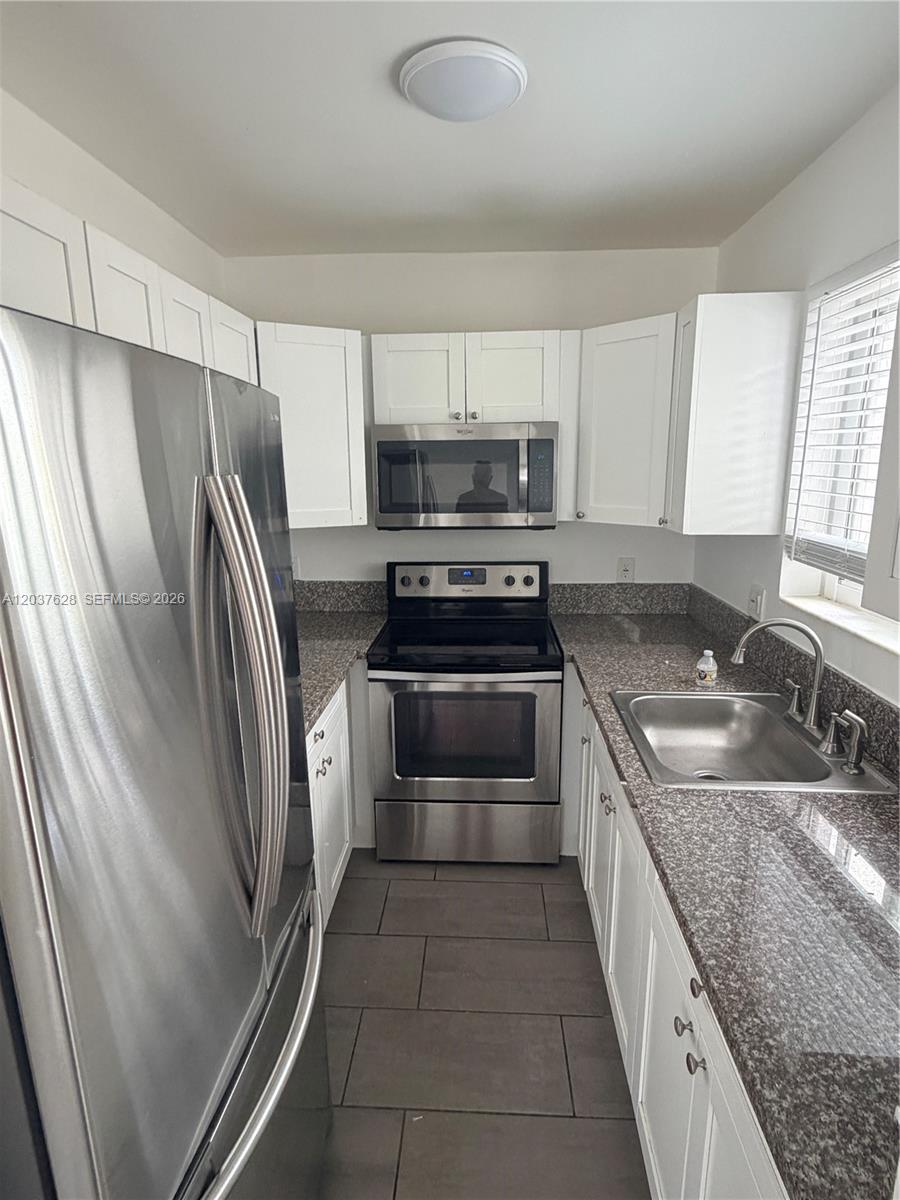 A galley kitchen features white cabinets, stainless steel appliances, and dark granite countertops — 1315 N 22nd Ave # A2, Hollywood FL 33020, HOLLYWOOD, FL