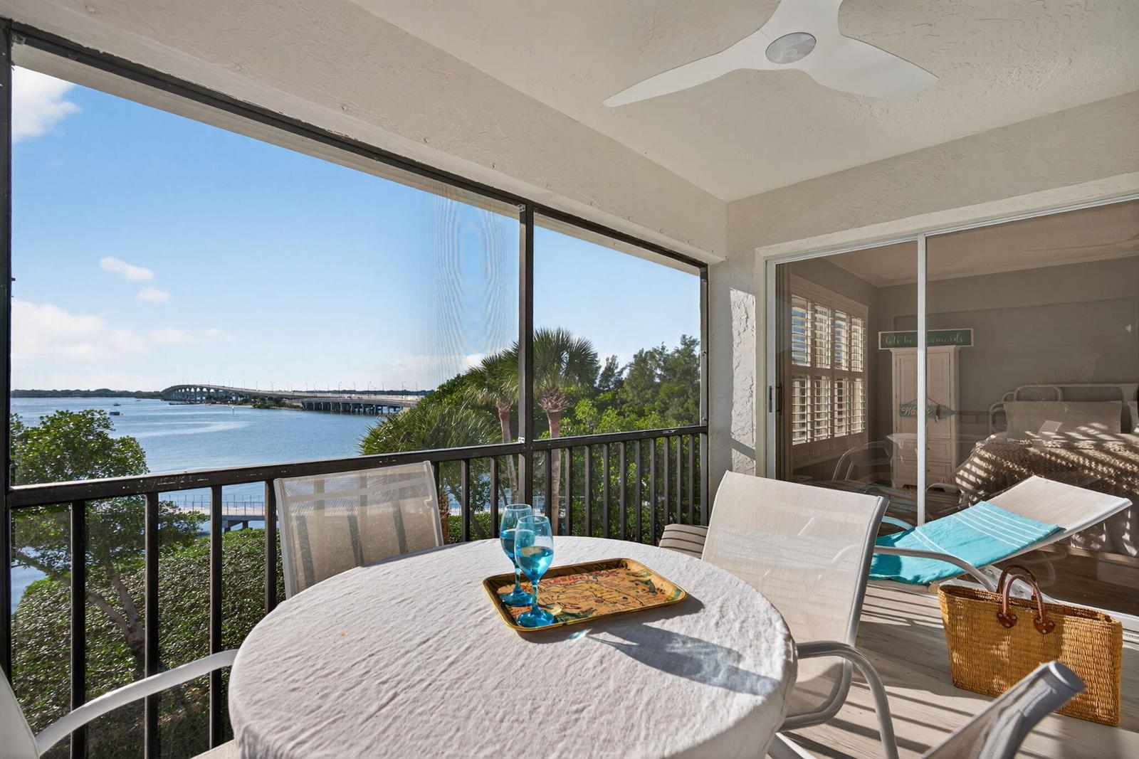 A screened-in balcony features a round table, chairs, and a view of a coastal bridge — 390 NE Edgewater Drive # 403, Stuart FL 34996, STUART, FL