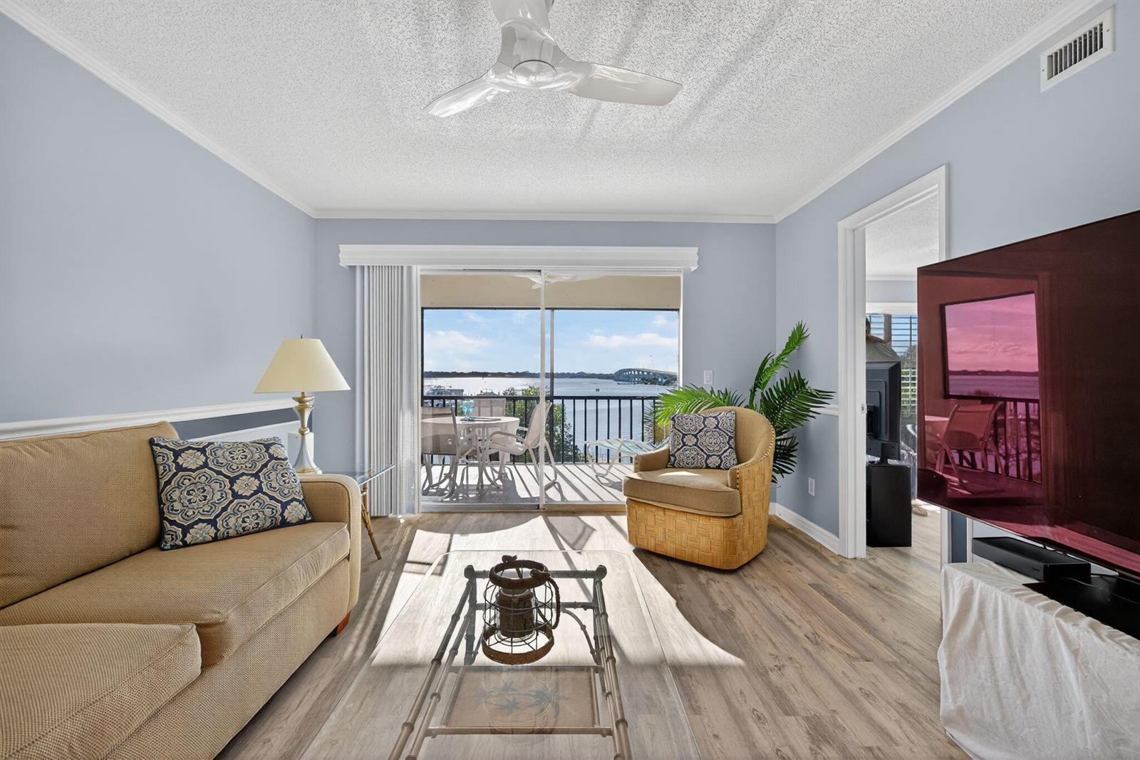 A living room features light blue walls, wood-look flooring, a sofa, and a balcony view — 390 NE Edgewater Drive # 403, Stuart FL 34996, STUART, FL