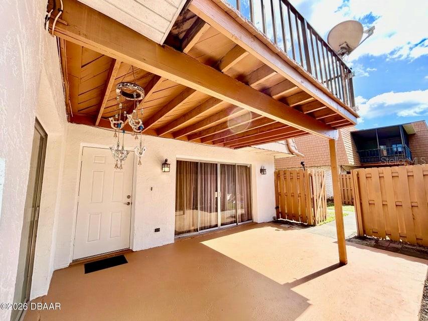 A covered patio features a white door, sliding glass doors, and a wooden balcony above — 122 MOONSTONE COURT, PORT ORANGE, FL
