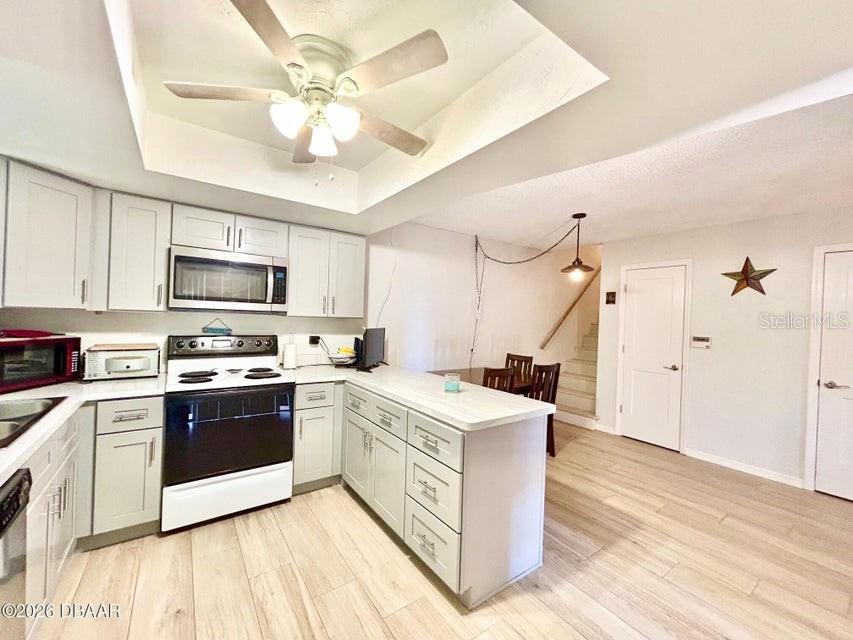 A kitchen features white cabinets, stainless steel appliances, and a peninsula with light countertops — 122 MOONSTONE COURT, PORT ORANGE, FL