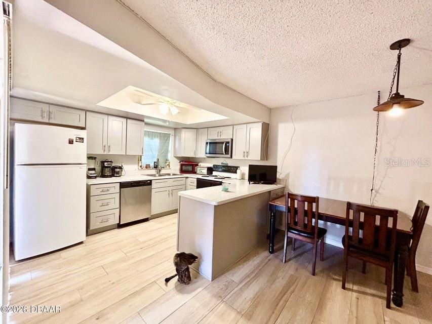 A kitchen features light-colored cabinetry, stainless steel appliances, a peninsula, and a dining area — 122 MOONSTONE COURT, PORT ORANGE, FL