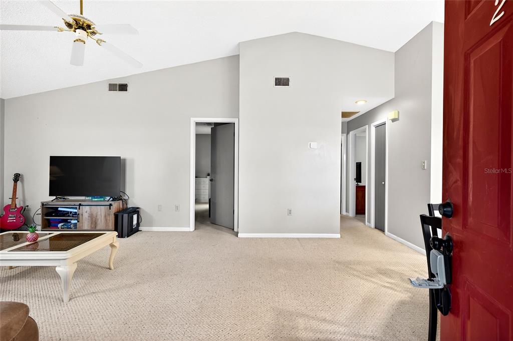 A living room with beige carpet, vaulted ceilings, a ceiling fan, and a red door — 2945 SW 32ND AVENUE UNIT D6, OCALA, FL