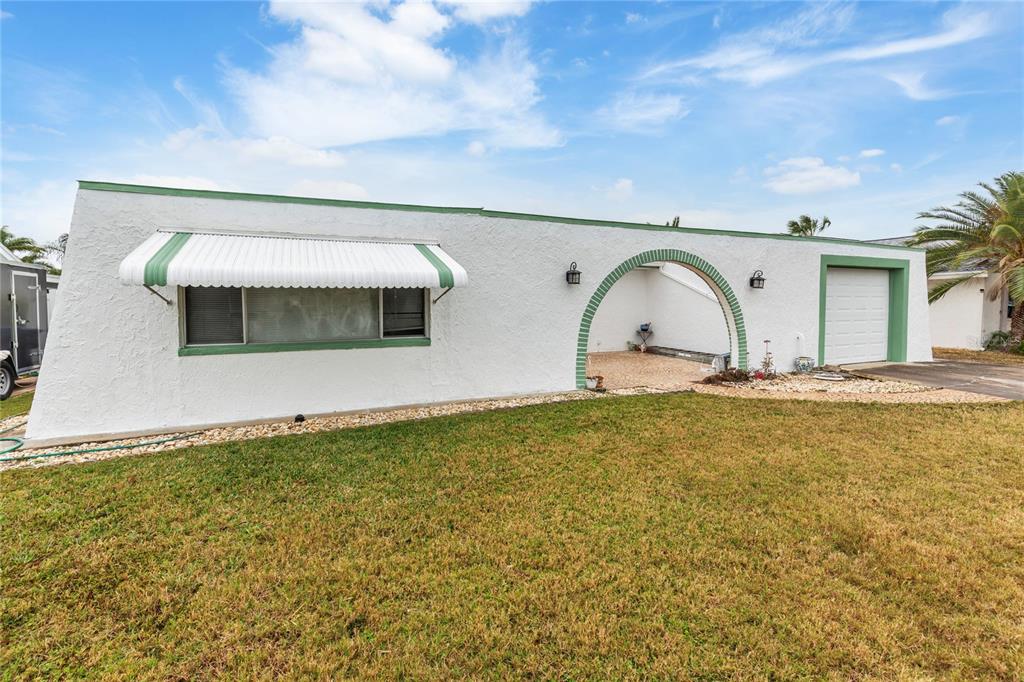 A white, single-story house with a green-trimmed arched entryway and a white metal awning — 3228 ROCK VALLEY DRIVE, HOLIDAY, FL