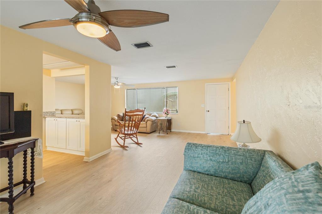 A living room features light wood-look flooring, a ceiling fan, and a teal patterned sofa — 3228 ROCK VALLEY DRIVE, HOLIDAY, FL