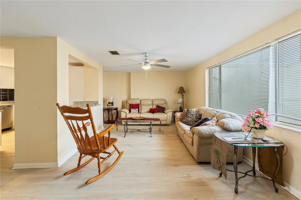 A living room features light-colored wood flooring, a ceiling fan, two sofas, and a rocking chair — 3228 ROCK VALLEY DRIVE, HOLIDAY, FL