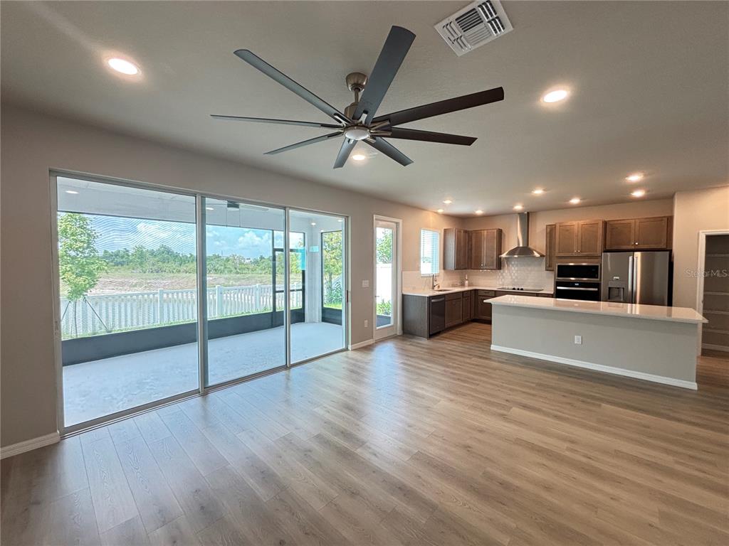 An open-concept kitchen and living area features wood-look flooring, a ceiling fan, and sliding doors — 3379 YELLOW CASSIA DRIVE, WESLEY CHAPEL, FL
