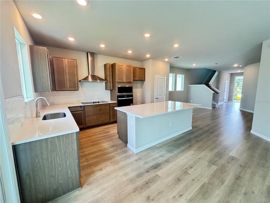 A modern kitchen features wood cabinets, white countertops, a central island, and light wood flooring — 3379 YELLOW CASSIA DRIVE, WESLEY CHAPEL, FL