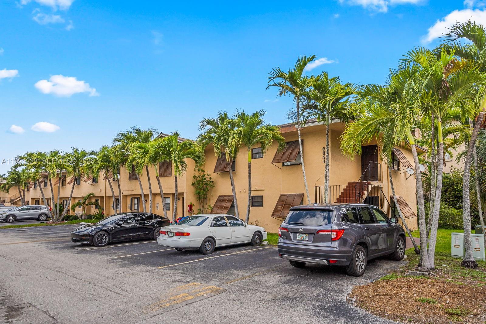 A two-story tan apartment building with palm trees and parked cars in the foreground — 6854 NW 173rd Dr # 210, Hialeah FL 33015, HIALEAH, FL