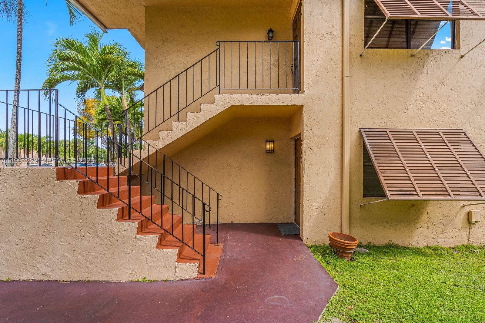 An exterior view of a tan building with an outdoor staircase leading to an upper unit — 6854 NW 173rd Dr # 210, Hialeah FL 33015, HIALEAH, FL