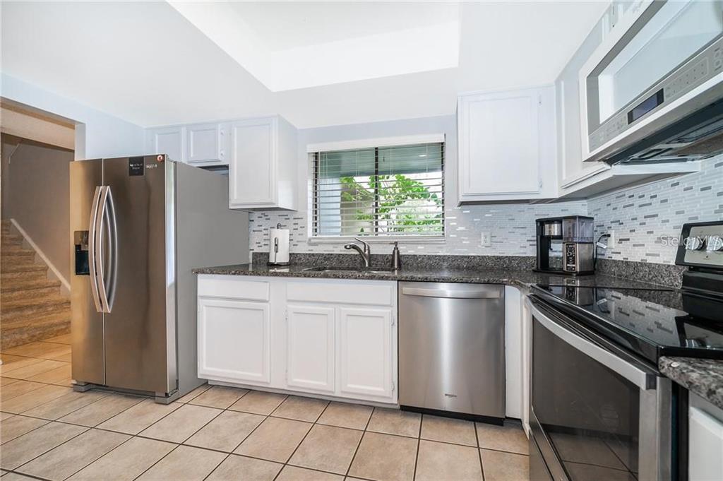 A kitchen with white cabinets, granite countertops, stainless steel appliances, and tile flooring — 7470 CANFORD COURT UNIT 23, WINTER PARK, FL