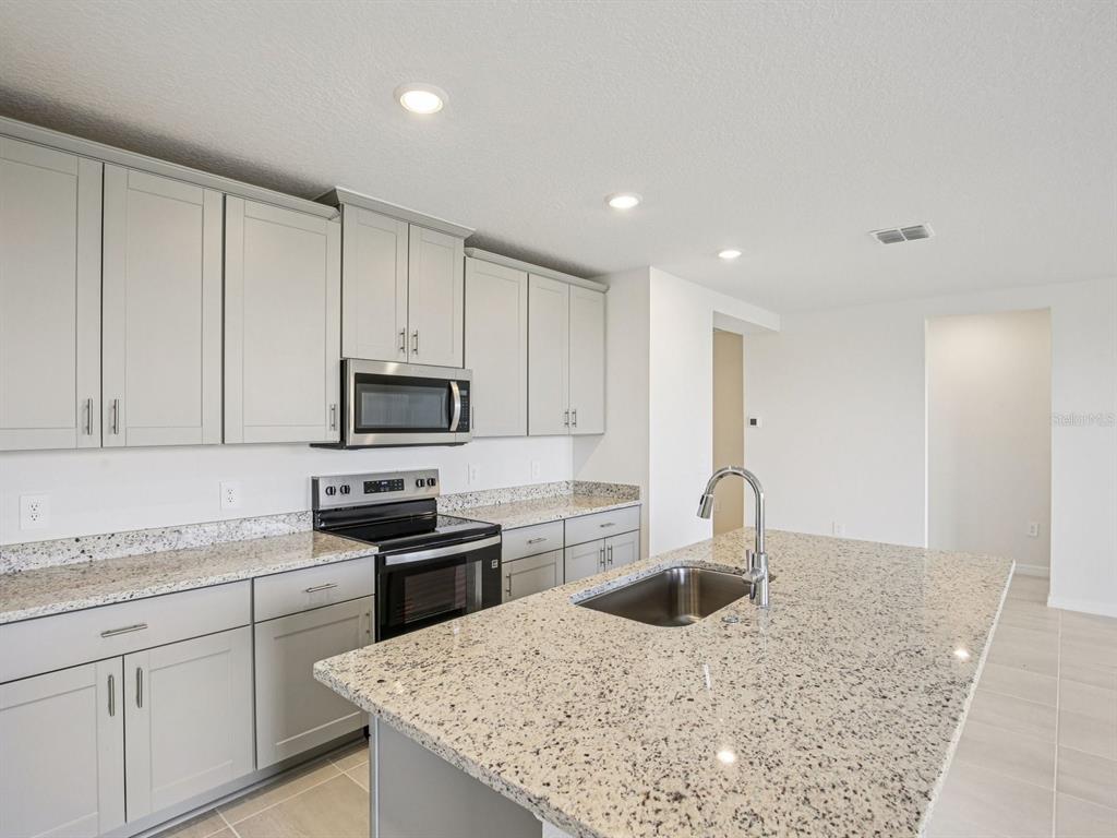 A modern kitchen features gray cabinets, granite countertops, stainless steel appliances, and a central island — 823 SUNSHOWER DRIVE, LADY LAKE, FL