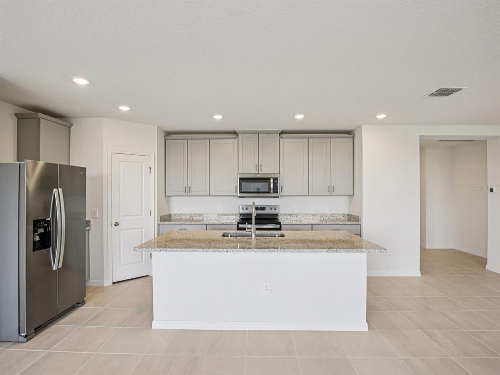 A kitchen features light gray cabinets, granite countertops, a central island, and stainless steel appliances — 823 SUNSHOWER DRIVE, LADY LAKE, FL