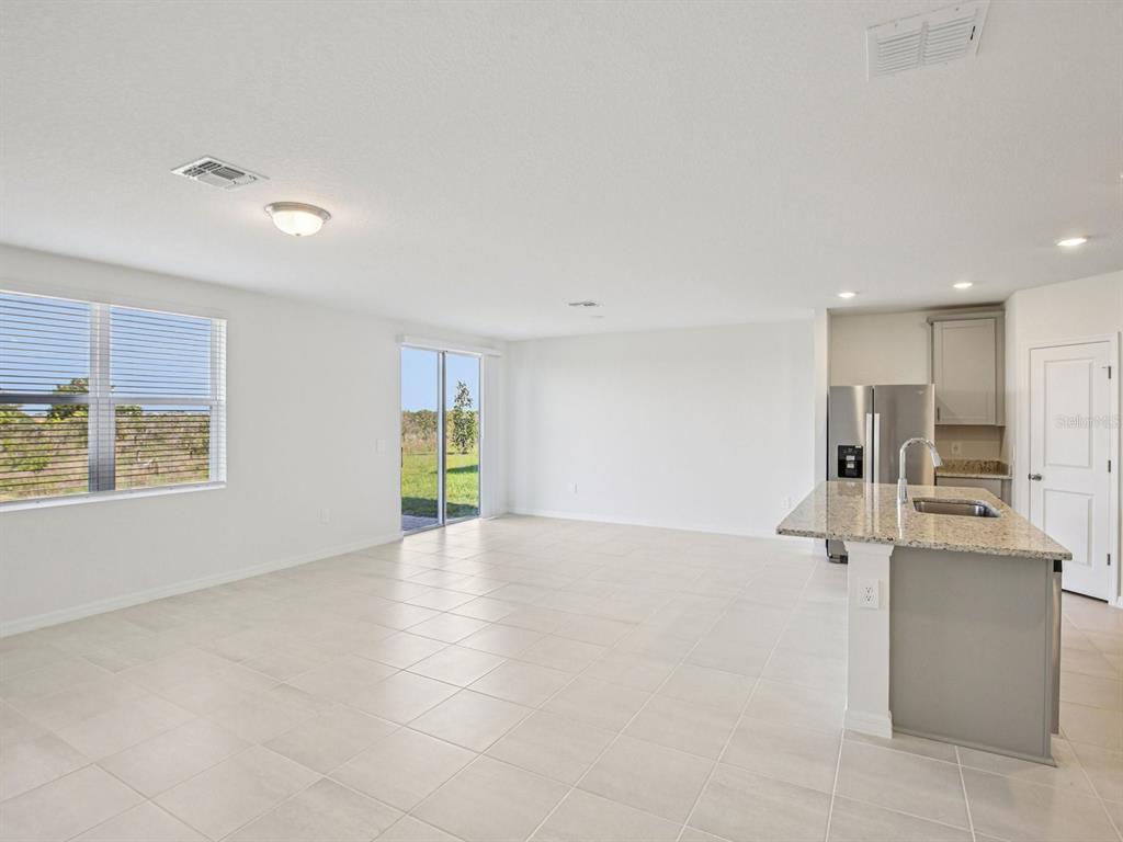 A bright, open-concept kitchen and living area with tile flooring and a sliding glass door — 823 SUNSHOWER DRIVE, LADY LAKE, FL