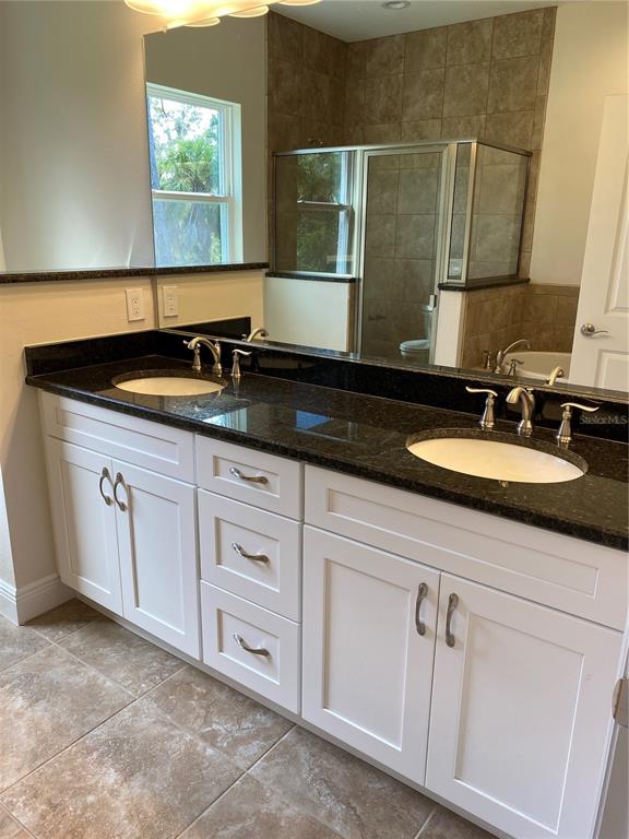 A bathroom features a double vanity with white cabinets, dark countertops, and a tiled shower — 1793 NAMATKA AVENUE, NORTH PORT, FL
