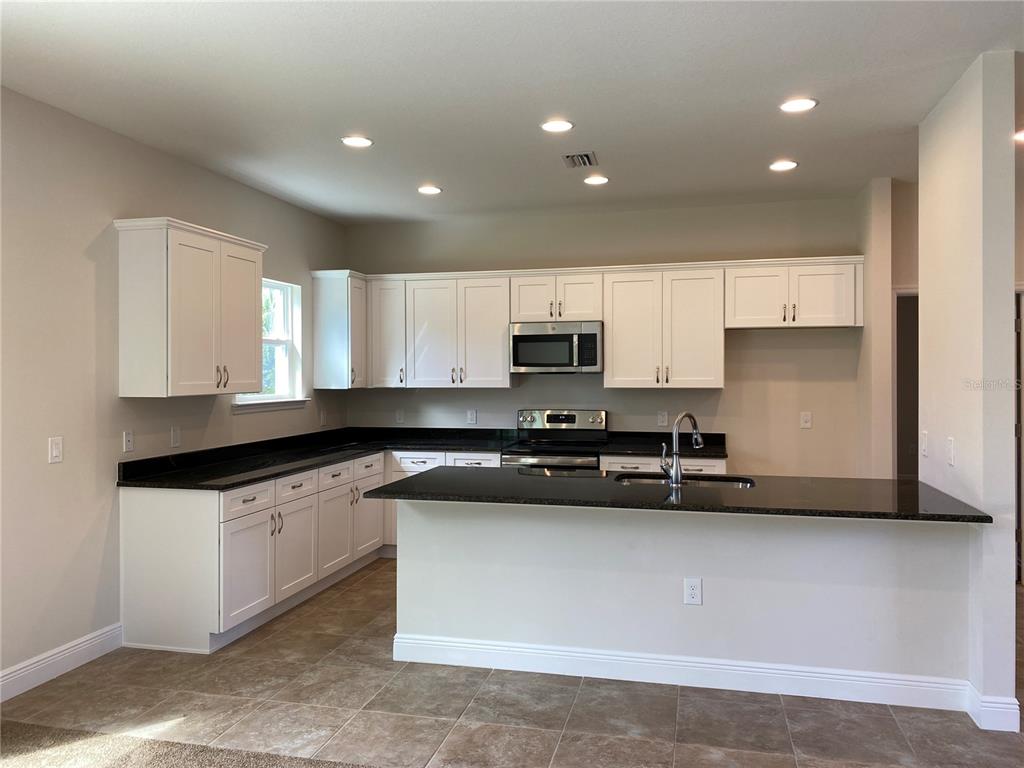 A kitchen with white cabinets, black countertops, stainless steel appliances, and tile flooring — 1793 NAMATKA AVENUE, NORTH PORT, FL