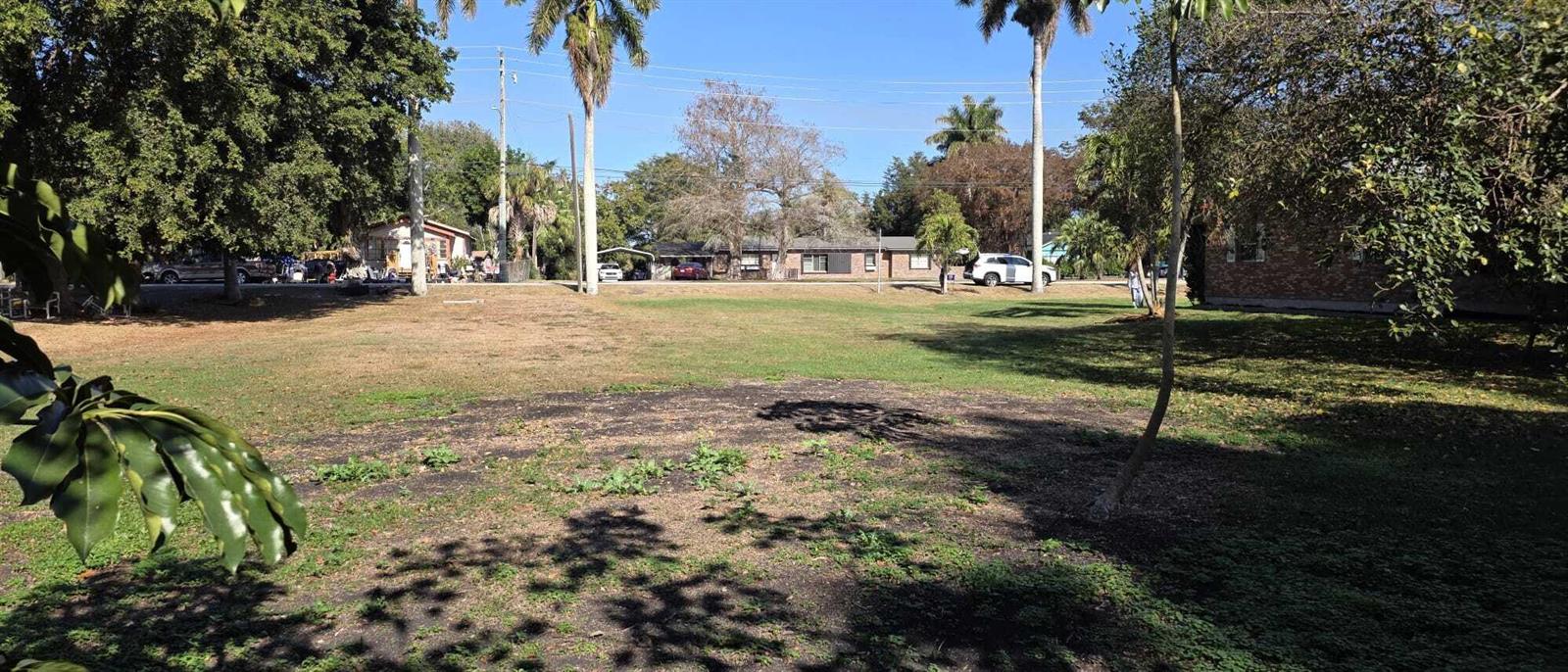 A large, grassy vacant lot with several trees and neighboring houses in the background — 00 Bacom Point Road, Pahokee FL 33476, PAHOKEE, FL