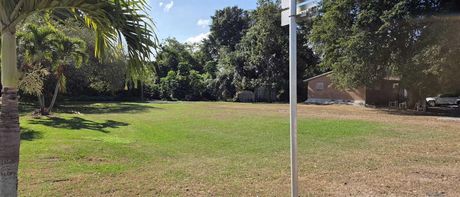 A large, grassy vacant lot features a palm tree, surrounding trees, and a neighboring house — 00 Bacom Point Road, Pahokee FL 33476, PAHOKEE, FL