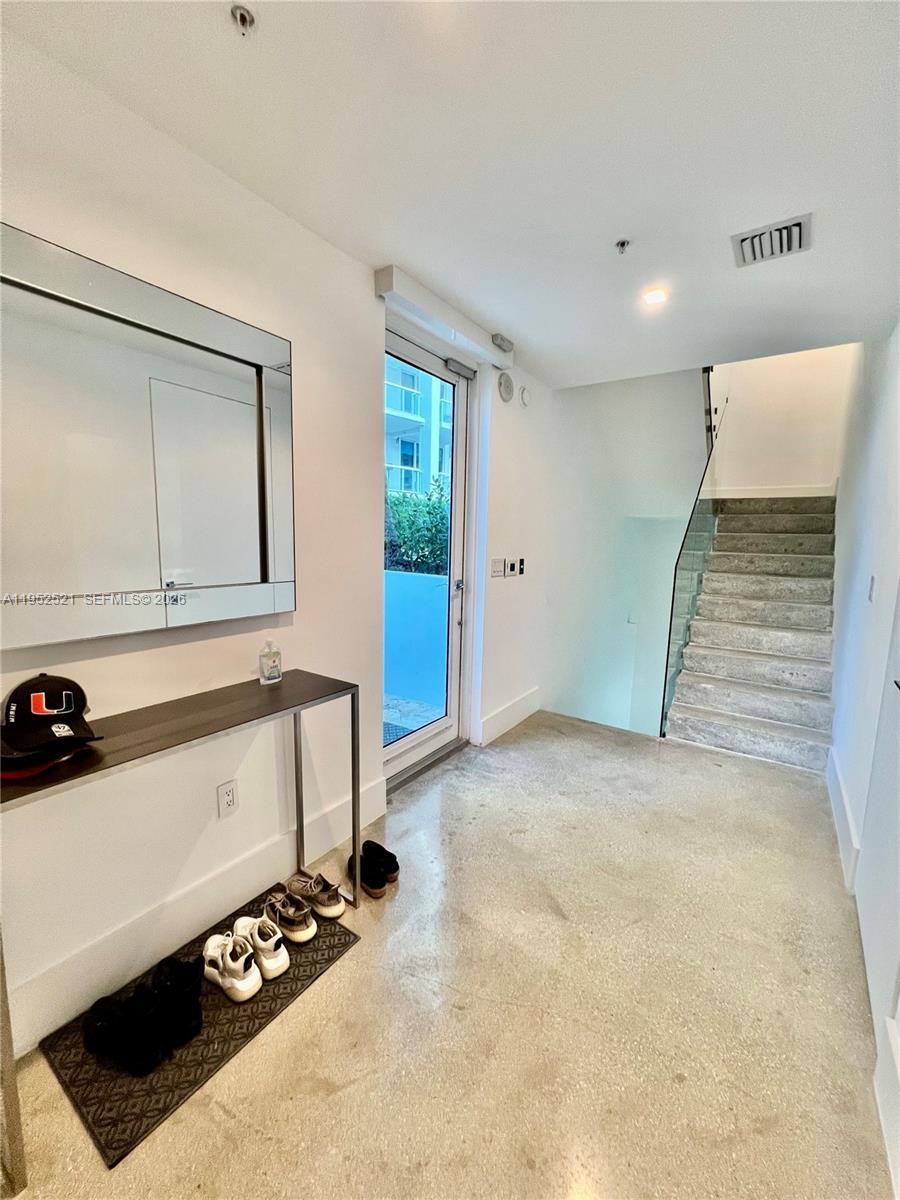 A modern entryway features a console table, a large mirror, and stairs with glass railings — 50 S Pointe Dr, Miami Beach FL 33139, MIAMI BEACH, FL