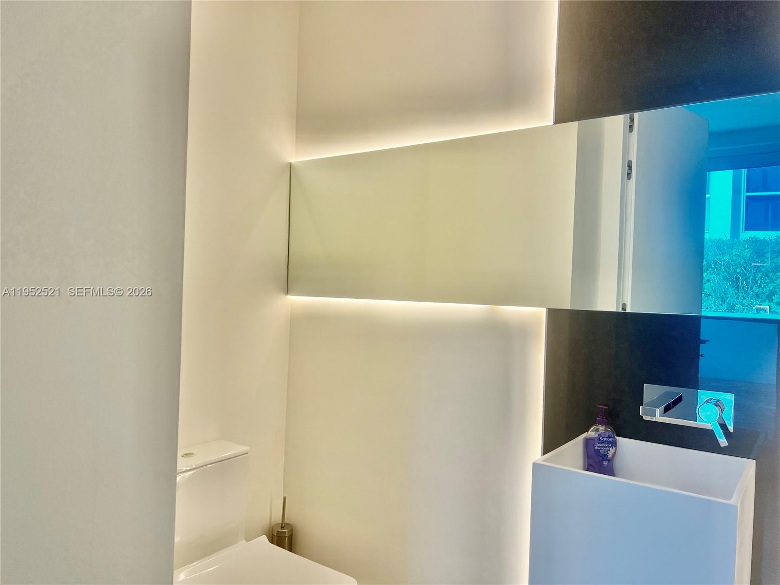 A modern bathroom features a wall-mounted sink, a toilet, and a backlit rectangular mirror — 50 S Pointe Dr, Miami Beach FL 33139, MIAMI BEACH, FL