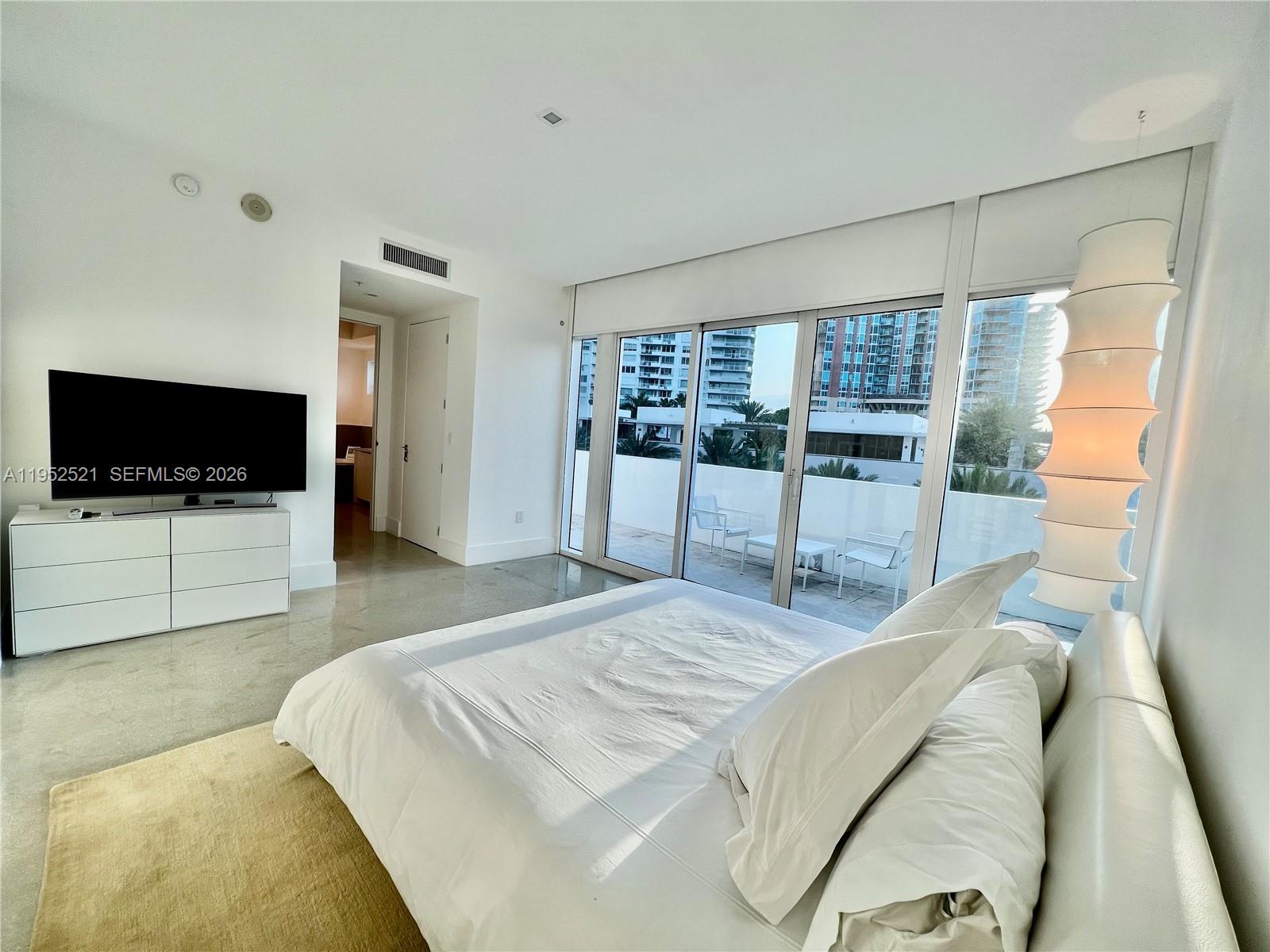 A modern bedroom features a white bed, concrete floors, and a balcony with city views — 50 S Pointe Dr, Miami Beach FL 33139, MIAMI BEACH, FL