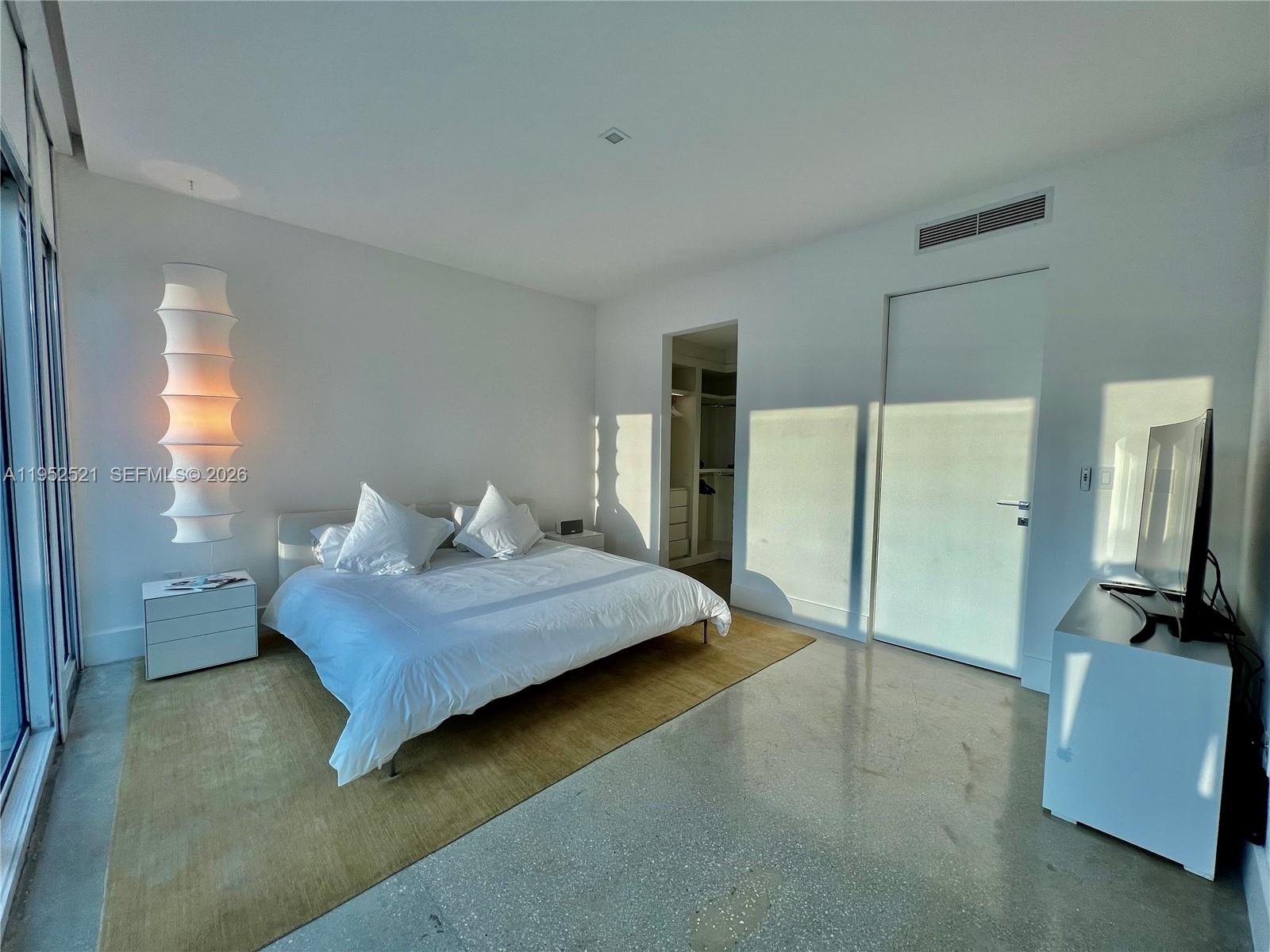 A modern bedroom features a bed on a rug, a tall lamp, and concrete floors — 50 S Pointe Dr, Miami Beach FL 33139, MIAMI BEACH, FL